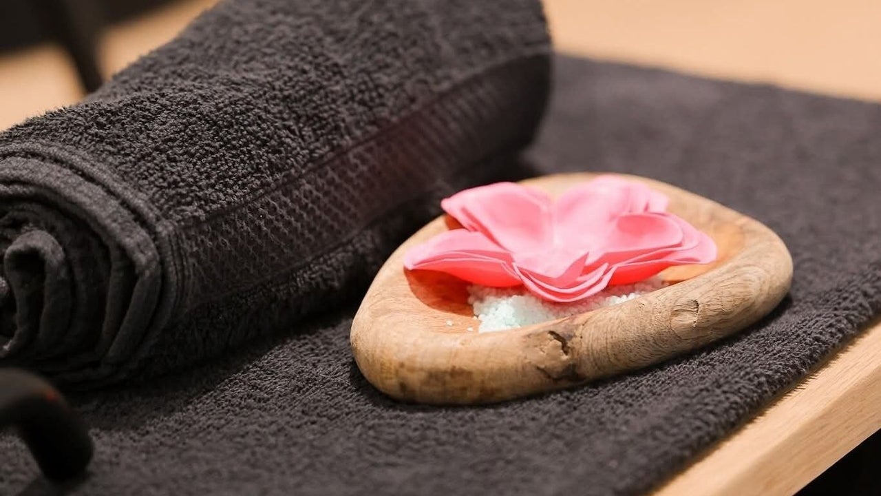 Opgerolde donkere handdoek met een stenen schaaltje vol roze bloemblaadjes, klaar voor een behandeling