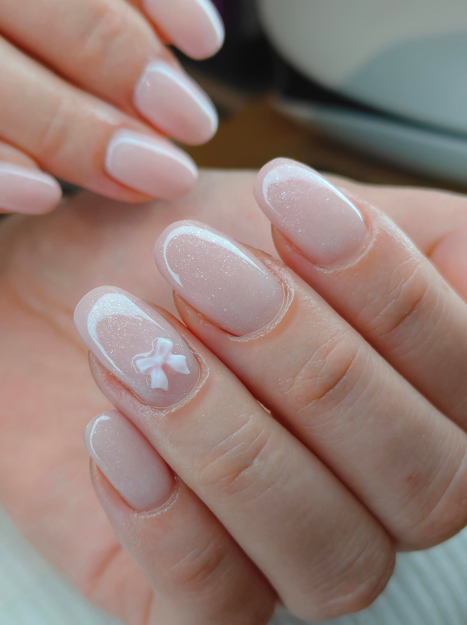 Nude nagels met glitter en een witte strik als accent